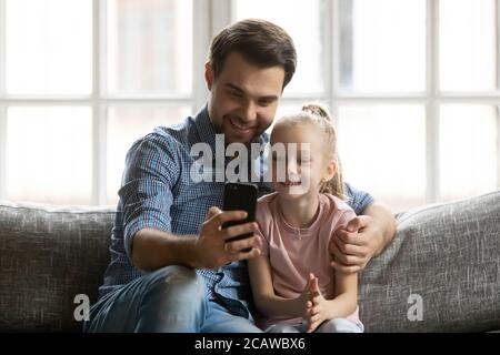 Junger Papa nimmt Selfie auf Handy mit kleiner Tochter. Stockfoto