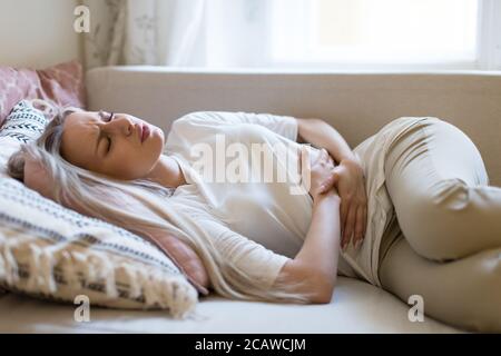 Gesundheitsprobleme Probleme.Junge kaukasische Frau, die an Magenschmerzen leidet, Bauchschmerzen oder Krämpfe fühlt, auf dem Sofa liegend.Menstruation der Periode, weiblich Stockfoto