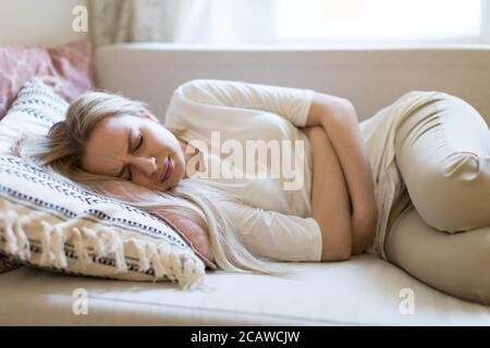 Gesundheitsprobleme Probleme.Junge kaukasische Frau, die an Magenschmerzen leidet, Bauchschmerzen oder Krämpfe fühlt, auf dem Sofa liegend.Menstruation der Periode, weiblich Stockfoto