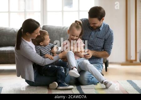 Verspielte junge Eltern kitzeln lachende kleine Tochter und Sohn. Stockfoto