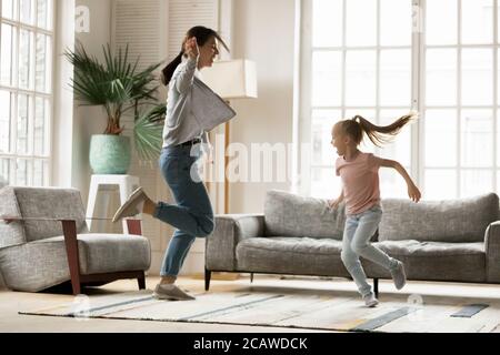 Energische junge Mutter tanzt mit kleiner Tochter zu Hause. Stockfoto