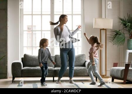 Fröhliche, energische junge Mutter, die mit kleinen Kindern zu Musik tanzt. Stockfoto