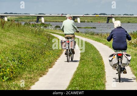 Kampen, Niederlande, 27. Juli 2020: Ältere Paare radeln auf einem Betonweg entlang des neuen Reevdiep-Flusskanals Stockfoto