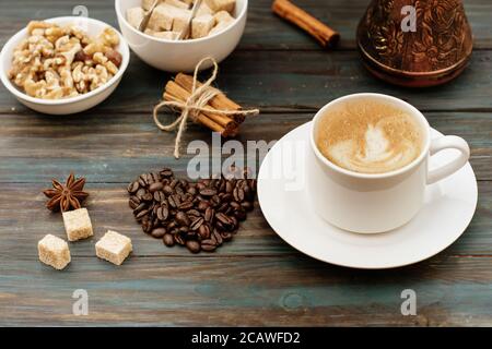 Nüsse in der Schüssel, Kaffeekanne, herzförmige Kaffeebohnen, Zimt, Anis, Zucker und Kaffeekappe auf Holzboden Stockfoto