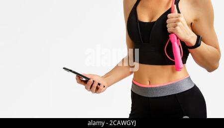 Sportliche Frau prüft Fitness-Tracker mit Smartphone auf weißem Hintergrund. Cardio-Workout-Konzept. Stockfoto