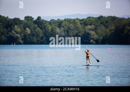 Freiburg, Deutschland. August 2020. Eine Frau reitet auf einem Stand Up Paddle Board (SUP) über den Opfinger See. Die sommerlichen Temperaturen ziehen viele Menschen an die Badeseen, aber weniger als befürchtet. Laut DLRG ist die Zahl der landesweiten Badetodesfälle im Vergleich zum Vorjahr gesunken. Quelle: Philipp von Ditfurth/dpa/Alamy Live News Stockfoto