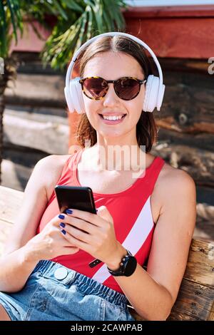 Junge lächelnde Frau sitzt auf Holzbank und genießt Musik Im Sommerresort Stockfoto