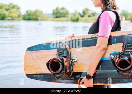 Aktiver junger Surfer in Sportbekleidung hält Surfboard im Stehen Am Wasser Stockfoto