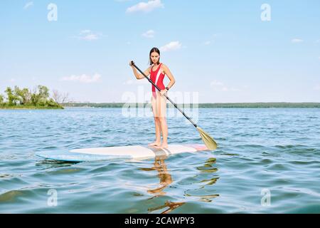Junge hübsche Brünette Sportlerin in rotem Badeanzug schwimmend auf Surfbrett Stockfoto