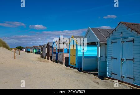 Reihe von bunten Strandhütten an einem Sandstrand in hellem Sonnenlicht. Stockfoto