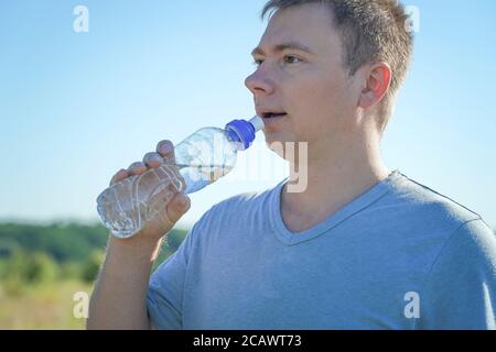 Ein Typ mit Brille und T-Shirt hält einen Kunststoff Wasserflasche in den Händen Stockfoto