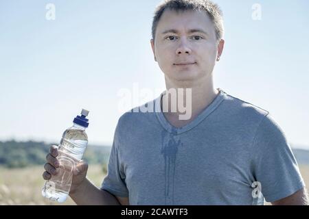 Ein Typ mit Brille und T-Shirt hält einen Kunststoff Wasserflasche in den Händen Stockfoto