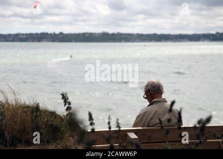 Ein älterer Mann sitzt allein auf einer Bank mit Blick auf das Meer im Lepe Country Park, Hampshire, England, Großbritannien, August 2020 Stockfoto