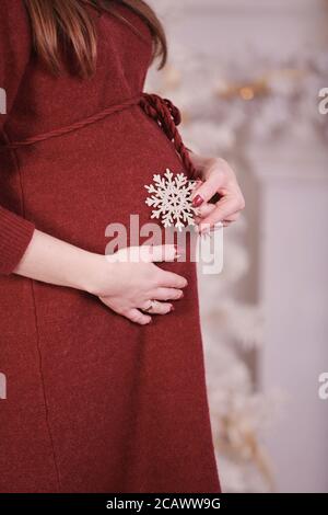 Schwangere Frau in der Nähe des Weihnachtsbaums. Bauch aus nächster Nähe Stockfoto