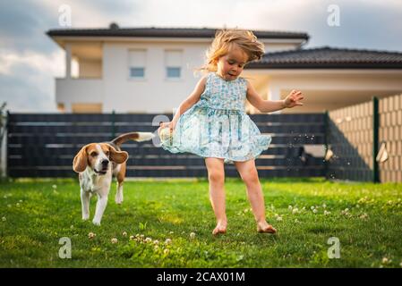 Baby Mädchen laufen mit Beagle Hund im Garten am Sommertag. Haustiere mit Kindern Konzept. Stockfoto