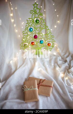 Vertikale Aufnahme von Geschenken in Bastelpapier und Band eingewickelt Auf Stoff mit Weihnachtsbaum Stockfoto