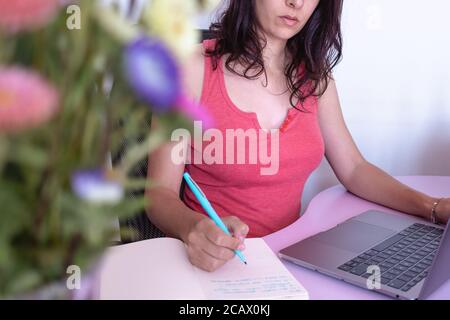 Junge Brünette kaukasischen Mädchen in Freizeitkleidung sitzen vor einem Schreibtisch mit Laptop Schreiben auf einem Notebook, von zu Hause aus arbeiten, Surfen im Internet o Stockfoto