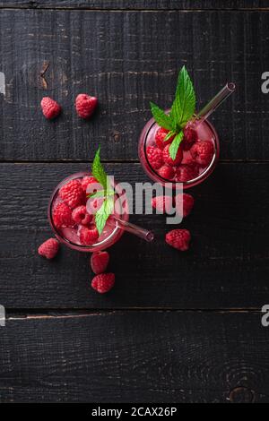 Frisch eiskalter Beerensaft-Drink mit Minze, Sommerlimonade in zwei Gläsern mit Strohhalmen auf dunklem Holzhintergrund, Draufsicht Stockfoto