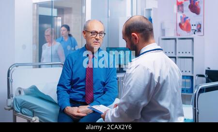 Senior Mann Beratung mit Arzt auf Krankenhausbett sitzen. Kranke ältere Patienten suchen medizinische Beratung für die Prävention von Krankheiten von Allgemeinmediziner in modernen Privatklinik, Arzt Diagnose Stockfoto