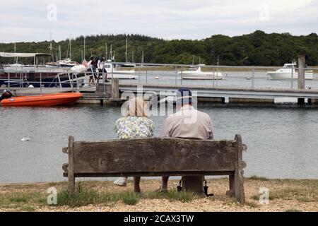 Ein älteres Paar sitzt auf einer Bank mit Blick auf Beaulieu River bei Bucklers Hard, Boldre, New Forest, Hampshire, England, Großbritannien Stockfoto