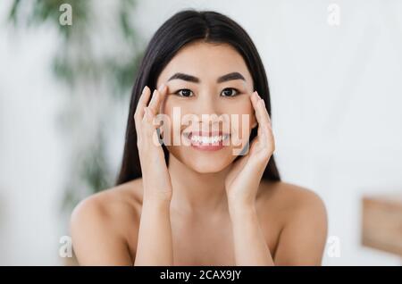 Attraktive lächelnde asiatische Frau reiben massieren ihre Augenzone Stockfoto