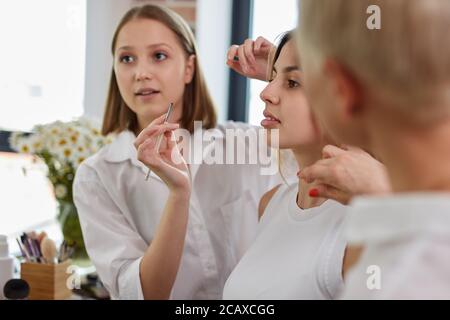 Prozess der Herstellung Make-up in Schönheitssalon. Visagiste arbeiten mit Pinsel auf Modell Gesicht. Anwendung Ton auf die Haut. Professionelle Make-up Künstler malt Modell Stockfoto