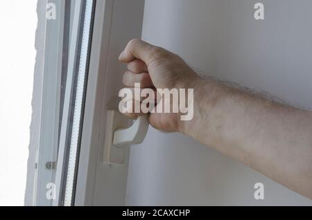 Männliche Hand öffnet das Fenster am Griff. Lüftung des Zimmers. Erwachsener kaukasischer Mann. Selektiver Fokus. Stockfoto