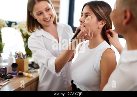 Prozess der Herstellung Make-up in Schönheitssalon. Visagiste arbeiten mit Pinsel auf Modell Gesicht. Anwendung Ton auf die Haut. Professionelle Make-up Künstler malt Modell Stockfoto