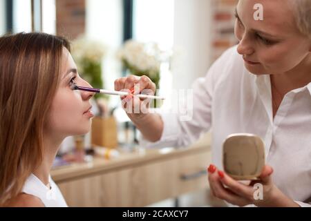 Professonal kaukasischen Visagist gelten Pulver auf Mädchen Gesicht mit der Verwendung von Pinsel. Prozess der Make-up zu tun Stockfoto