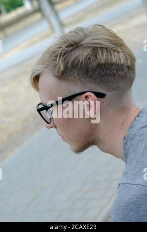 Porträt eines jungen kaukasischen Mannes mit Brille. Seitenansicht einer Blondine auf einer Bank auf einer Stadtstraße. Lifestyle. Selektiver Fokus. Stockfoto