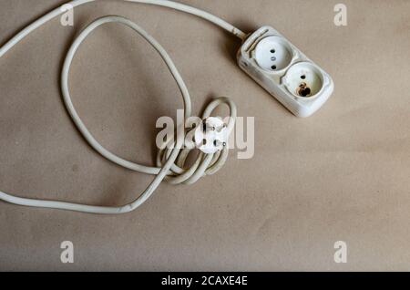 Elektrischer Stecker Zustand, Steckdose nach Schock auf braunem Hintergrund. Weiße Steckdosenleiste nach Kurzschluss. Elektrische Sicherheit. Stockfoto