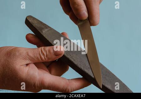 Die Hände des Menschen schärfen ein kleines Messer auf einem Schleifstein. Der Prozess des manuellen Schleifens eines Schneidwerkzeugs. Mann mittleren Alters der europäischen Rasse. Hand auch Stockfoto