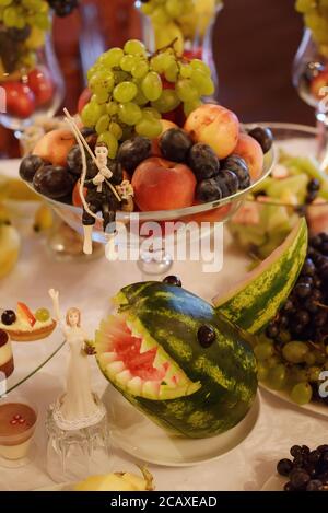 Hochzeitsbuffet mit frischem Obst und Kuchen. Verspielte Obstschnitzerei mit Kuchenform Figuren: Bräutigam Angeln die Braut vor dem Hai platziert Stockfoto