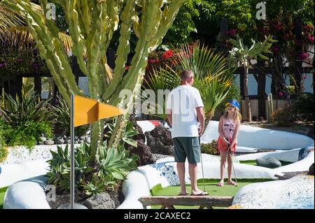 Vater und Tochter spielen gemeinsam Minigolf im tropischen Park, umgeben von Kakteen und Wasserspielen, Las Americas, Teneriffa, Spanien Stockfoto