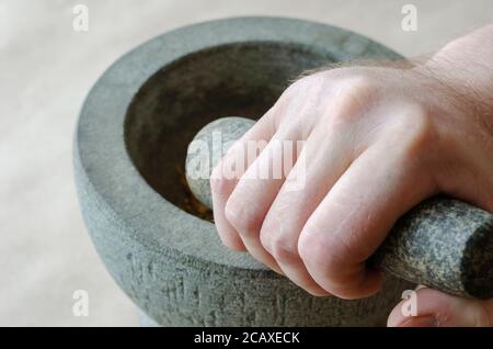 Die getrockneten Wurzeln der Heilkräuter werden von Hand in Steinmörtel gemahlen. Kaukasischer Mann mittleren Alters. Alternative Medizin. Heilkräuter. Stockfoto