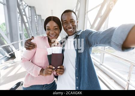 Zusammen Reisen. Glückliches afrikanisches Paar, das Selfie am Flughafen macht und auf das Boarding wartet Stockfoto