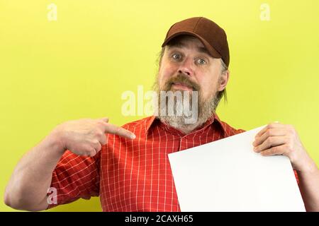 Männlicher Bauarbeiter mit leerer Werbetafel. Ein unhöflicher, bärtiger, strenger Mann in einem roten Hemd und einer Baseballmütze zeigt eine Nachricht Stockfoto