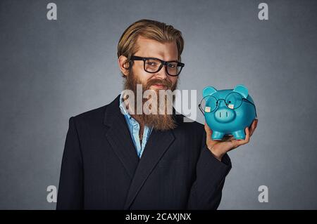 Closeup Portrait Kopf geschossen Junge schwere lächelt glücklich hipster Geschäftsmann holding Piggy Bank sowohl Brillen isoliert auf Grau studio Wand backgr Stockfoto