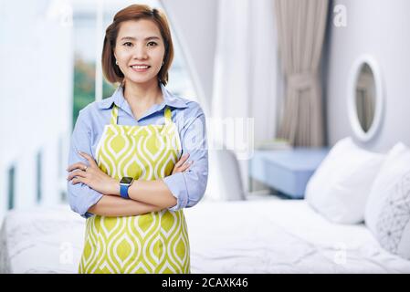 Porträt einer glücklichen jungen asiatischen Frau in Schürze über die Arme Und Blick auf die Kamera Stockfoto