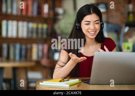 Lächelnde asiatische Frau im Headset mit Videokonferenz auf Laptop Stockfoto