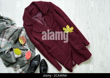 Bordeaux Mantel, Schal, schwarze Stiefel und Herbstblätter. Modisches Konzept Stockfoto