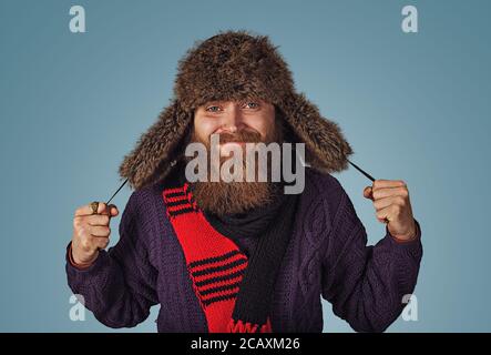 Bärtiger Mann Holding mit flauschigen Fell hat in roten Schal lila Pullover auf Blau studio Wand Hintergrund isoliert. Positive Gesichtsausdruck menschliche Emotion Stockfoto