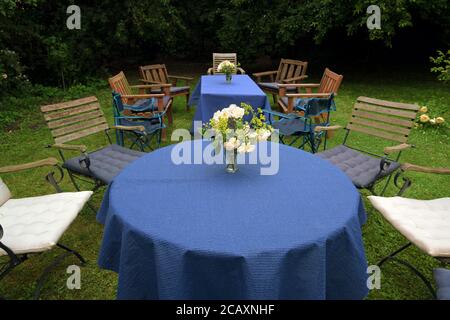 Richten Sie sich für eine Familie Gartenparty mit Tischen, blauen Tischdecken und verschiedenen Stühlen auf dem Rasen in einem ländlichen Hinterhof, ausgewählten Fokus Stockfoto
