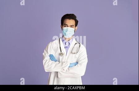 Zuversichtlich indischen Arzt trägt medizinische Maske und Gummihandschuhe über Lila Hintergrund Stockfoto