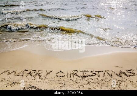 „Frohe Weihnachten“ steht im Sand am Strand, als die Wellen am 24. Dezember 2012 in Dauphin Island, Alabama, zusammenbrechen. Stockfoto