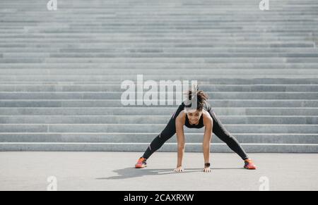 Übungen für Flexibilität. Fröhliche afroamerikanische Mädchen in Sportswear mit Fitness-Tracker tun Stretching Stockfoto