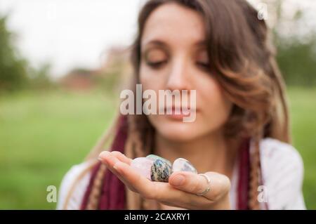 Junge schöne Mädchen mit langen Dreadlocks hält in den Händen 5 natürliche Steine Rosenquarz, Strass, Angelit, Anyolit und Azurit im Freien während Stockfoto