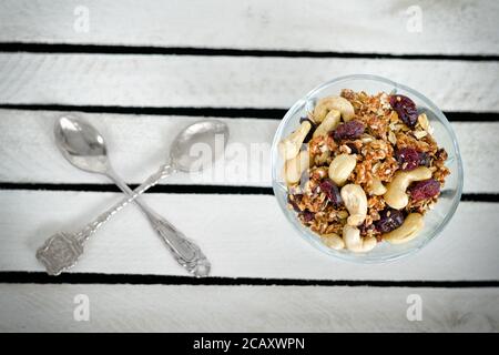 Piala mit Granola und zwei gekreuzten Löffeln auf einer weißen Holzkiste. Nahaufnahme Stockfoto