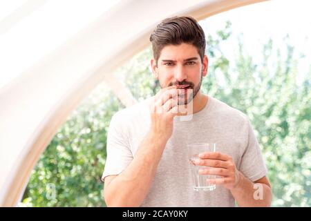 Ein hübscher Mann hält ein Glas Wasser in der Hand, während er die Pille nimmt. Stockfoto