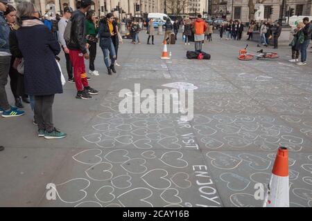 Touristen sahen, wie sie mit weißer Kreide auf dem Straßenbelag des Trafalgar Square, London, Großbritannien, von Straßenmusikern gezeichnete Herzen sahen. Stockfoto